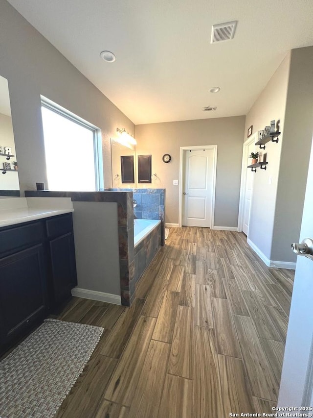 bathroom featuring a relaxing tiled tub, vanity, and hardwood / wood-style floors