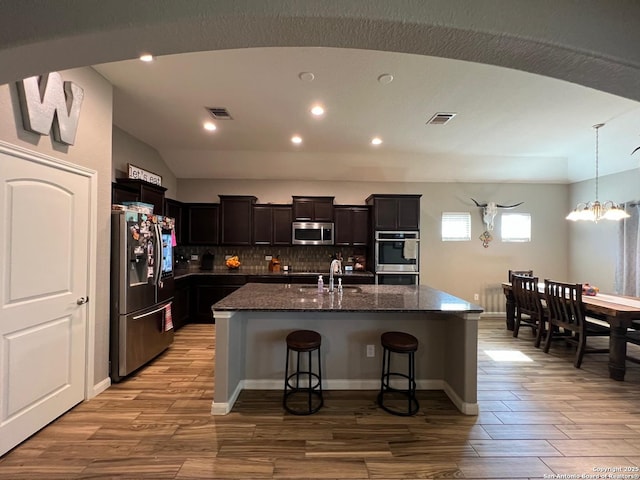 kitchen with appliances with stainless steel finishes, a breakfast bar, an island with sink, dark stone counters, and light hardwood / wood-style floors