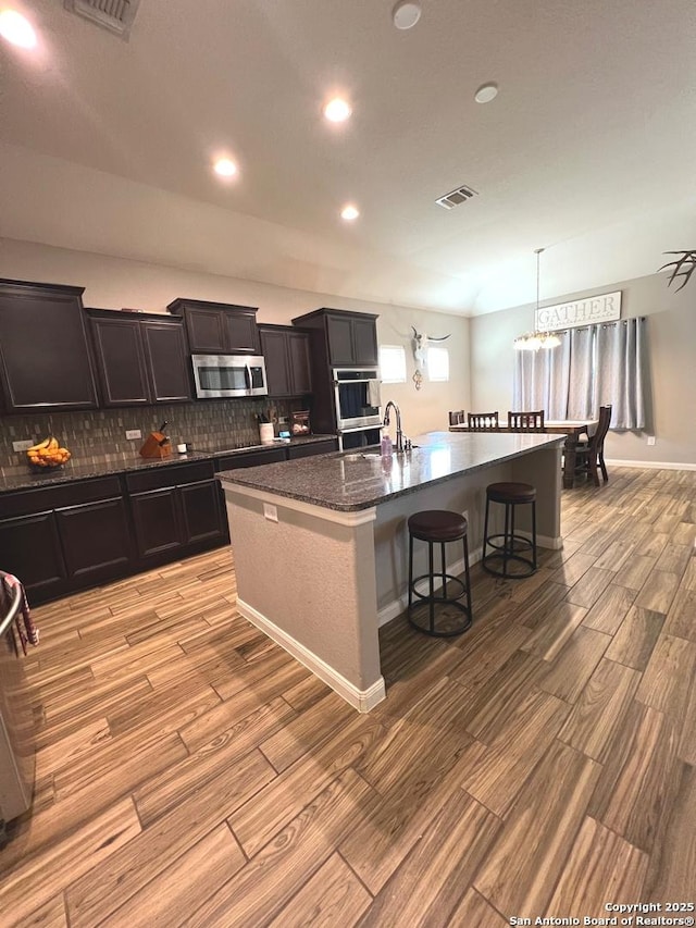 kitchen with a breakfast bar, light wood-type flooring, stainless steel appliances, a kitchen island with sink, and decorative backsplash