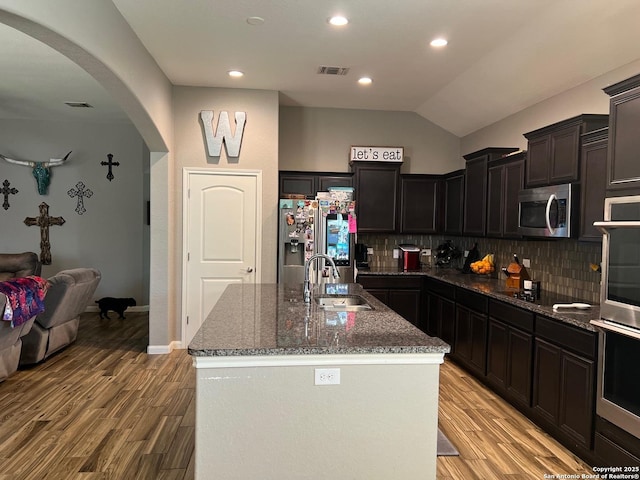 kitchen with stainless steel appliances, sink, light hardwood / wood-style floors, and an island with sink