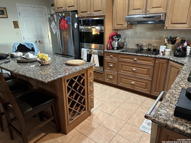 kitchen featuring appliances with stainless steel finishes, a breakfast bar, dark stone countertops, and light tile patterned floors