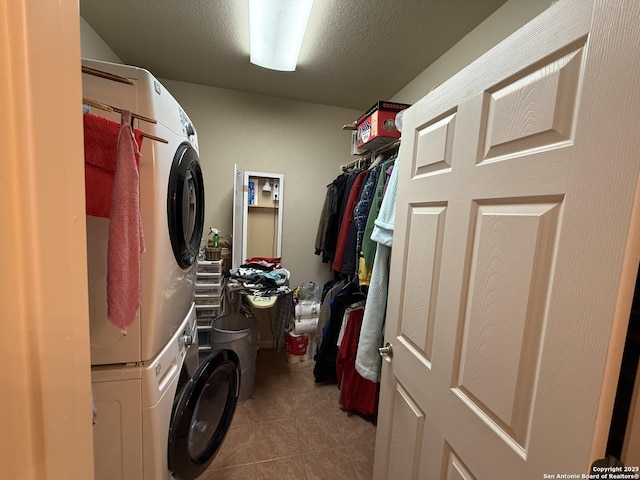 clothes washing area with stacked washer / dryer, a textured ceiling, and light tile patterned floors