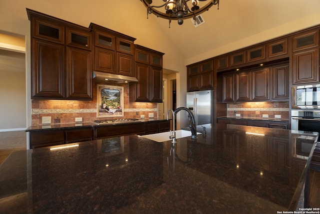 kitchen with sink, stainless steel appliances, dark brown cabinetry, decorative backsplash, and dark stone counters