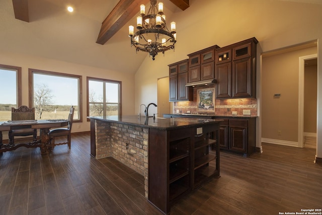 kitchen featuring dark wood-type flooring, dark brown cabinetry, tasteful backsplash, beam ceiling, and a kitchen island with sink