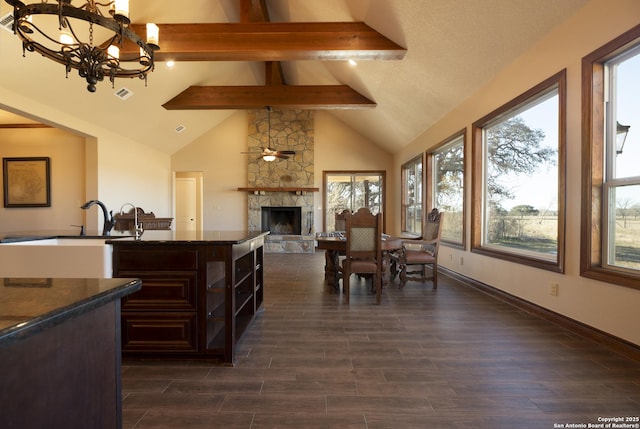 dining room featuring a stone fireplace, high vaulted ceiling, beamed ceiling, sink, and dark wood-type flooring