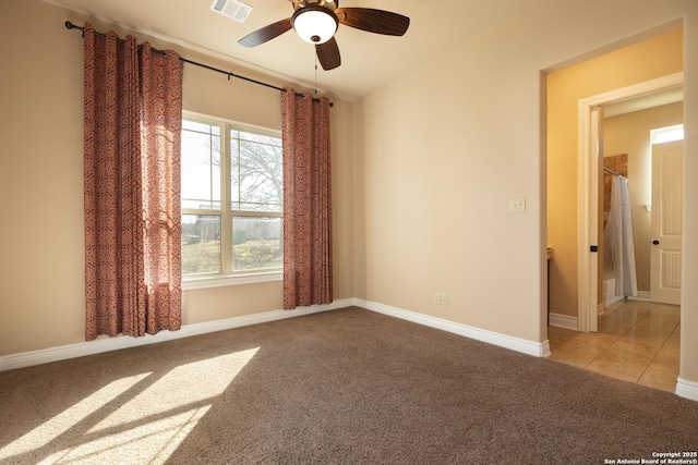 carpeted empty room featuring ceiling fan, tile patterned flooring, visible vents, and baseboards