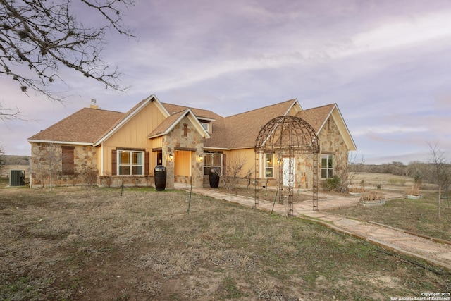 view of front of property with stone siding, a chimney, roof with shingles, central air condition unit, and a patio area