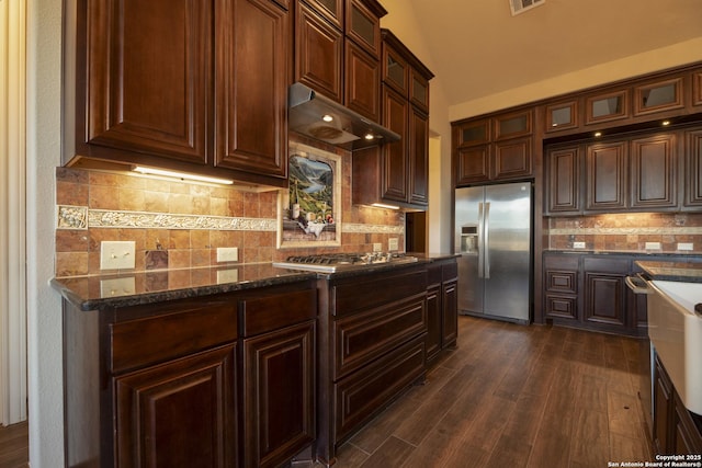 kitchen with appliances with stainless steel finishes, dark hardwood / wood-style floors, backsplash, and dark stone counters