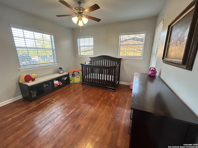 bedroom featuring a crib, dark wood-type flooring, and ceiling fan