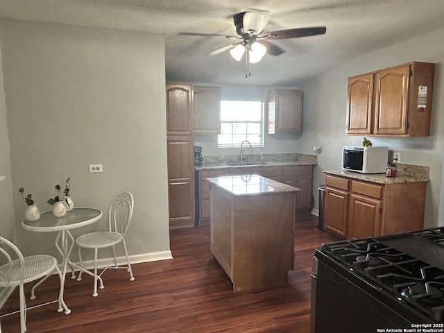 kitchen featuring dark wood-type flooring, sink, a center island, black gas range oven, and ceiling fan