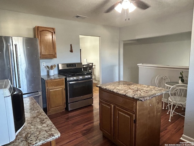 kitchen featuring dark hardwood / wood-style floors, a center island, ceiling fan, stainless steel appliances, and light stone countertops