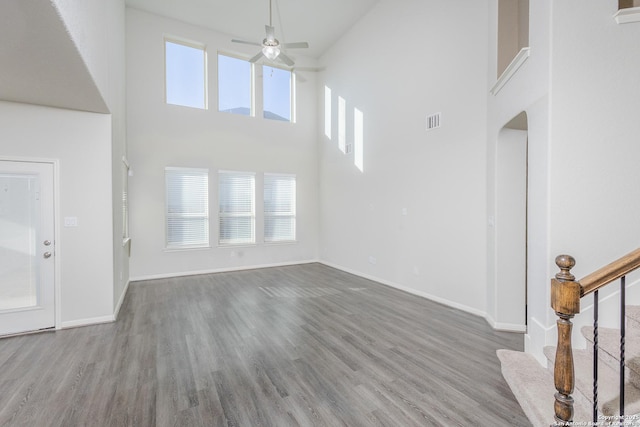 unfurnished living room with ceiling fan, hardwood / wood-style floors, and a towering ceiling