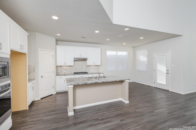 kitchen featuring white cabinetry, oven, light stone counters, and a center island with sink