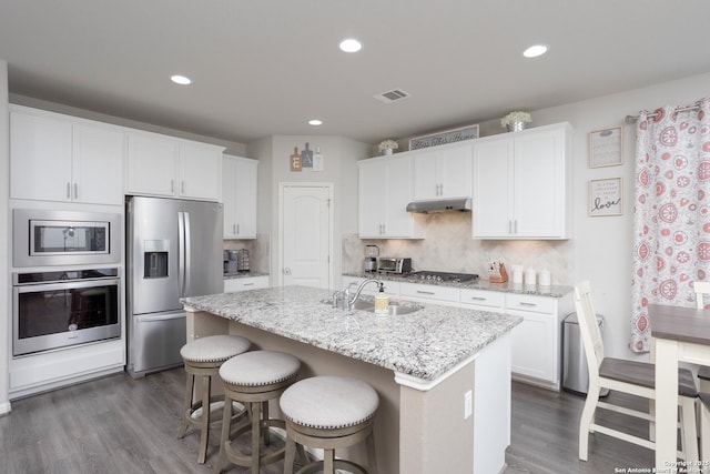 kitchen with white cabinetry, appliances with stainless steel finishes, an island with sink, and light stone counters