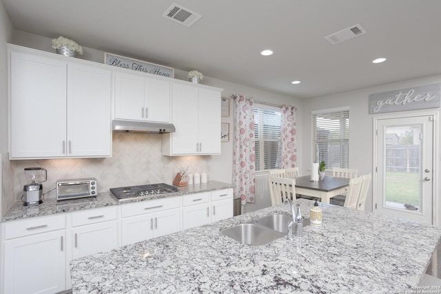 kitchen featuring stainless steel gas stovetop, white cabinetry, an island with sink, sink, and backsplash