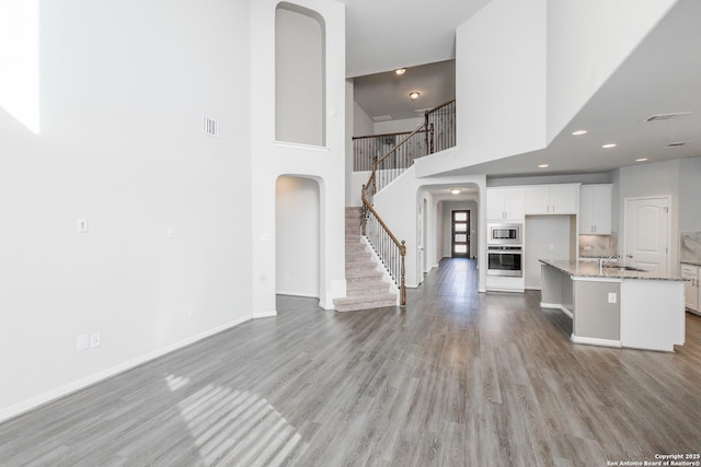 unfurnished living room with a towering ceiling, sink, and light wood-type flooring