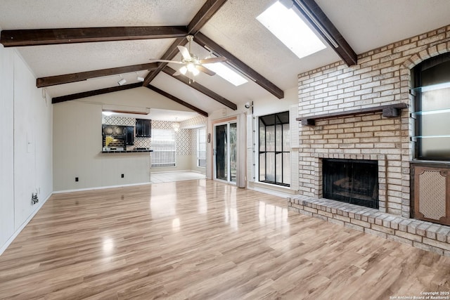 unfurnished living room featuring a fireplace, a textured ceiling, ceiling fan, vaulted ceiling with skylight, and light hardwood / wood-style floors