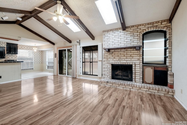 unfurnished living room with vaulted ceiling with beams, a fireplace, a textured ceiling, and light wood-type flooring