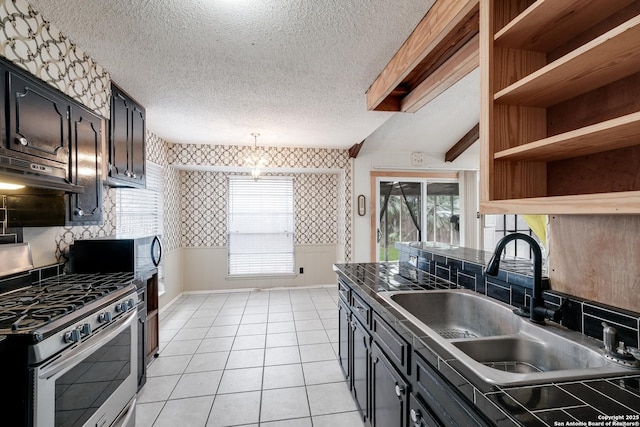 kitchen with sink, light tile patterned floors, stainless steel gas range oven, and a textured ceiling