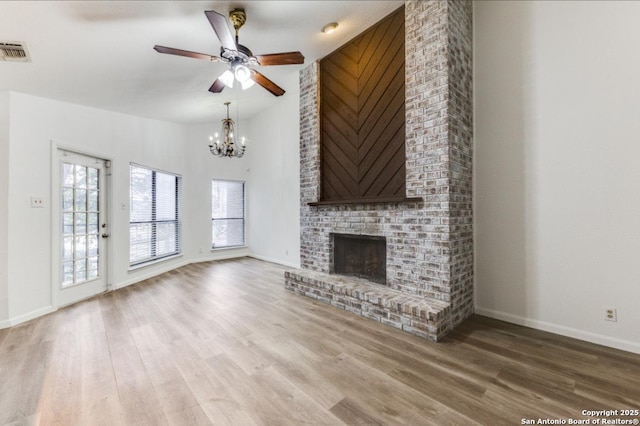 unfurnished living room with high vaulted ceiling, wood-type flooring, a fireplace, and ceiling fan with notable chandelier