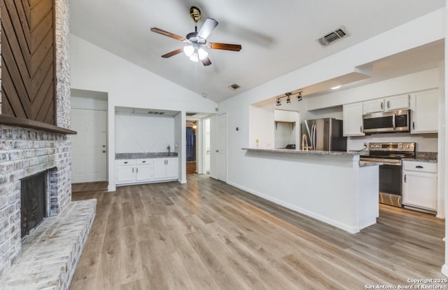 kitchen with white cabinets, light stone counters, kitchen peninsula, stainless steel appliances, and light wood-type flooring