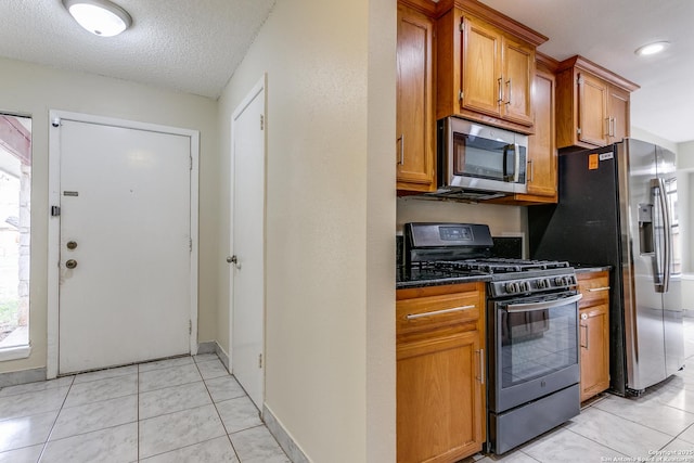 kitchen featuring stainless steel appliances, dark stone counters, a textured ceiling, and light tile patterned floors