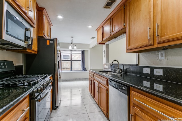 kitchen with dark stone countertops, sink, light tile patterned flooring, and appliances with stainless steel finishes