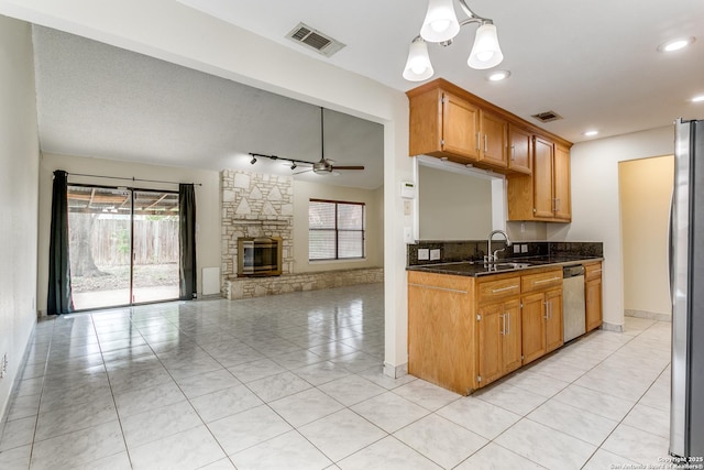 kitchen with light tile patterned floors, dark stone counters, ceiling fan, stainless steel appliances, and a fireplace