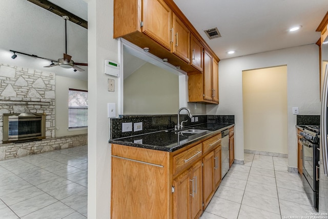 kitchen with a stone fireplace, sink, dark stone countertops, stainless steel dishwasher, and black range with gas stovetop