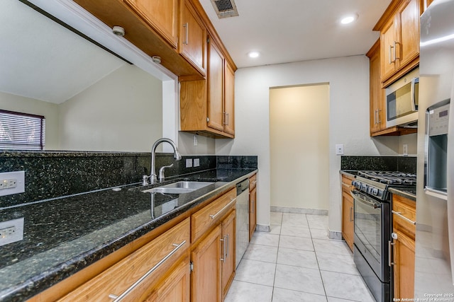 kitchen featuring appliances with stainless steel finishes, sink, dark stone countertops, and light tile patterned floors