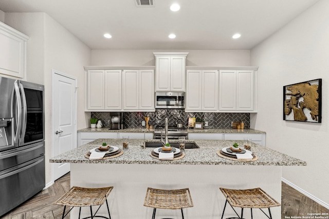 kitchen with stainless steel appliances, an island with sink, white cabinets, and a kitchen bar