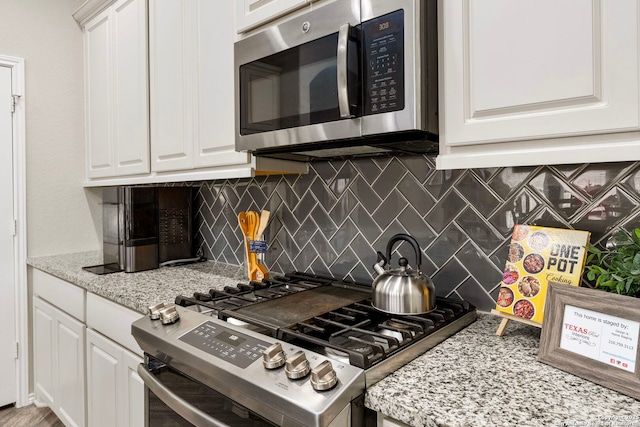 kitchen featuring white cabinetry, backsplash, light stone counters, and appliances with stainless steel finishes