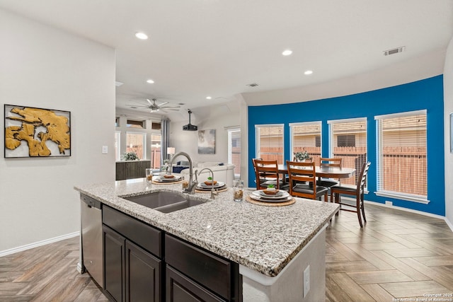 kitchen featuring sink, light parquet floors, light stone countertops, a center island with sink, and stainless steel dishwasher