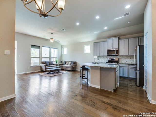 kitchen featuring appliances with stainless steel finishes, an island with sink, a breakfast bar area, gray cabinetry, and light stone countertops