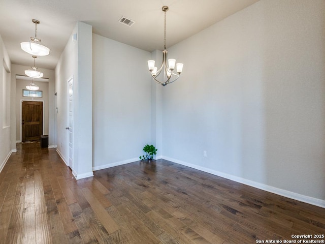 spare room with an inviting chandelier and dark hardwood / wood-style flooring