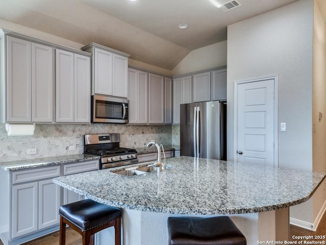 kitchen featuring an island with sink, appliances with stainless steel finishes, a kitchen bar, and sink