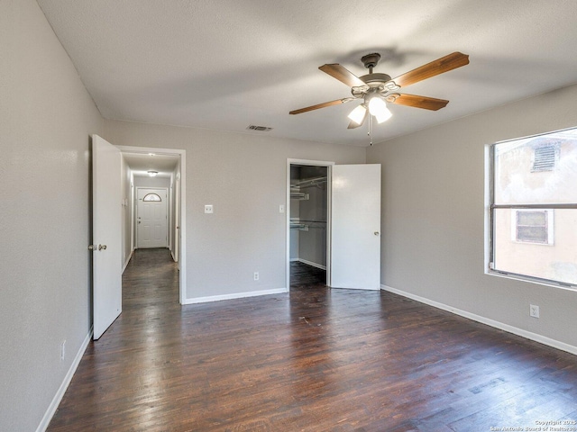 unfurnished bedroom with dark wood-type flooring, ceiling fan, a spacious closet, and a textured ceiling