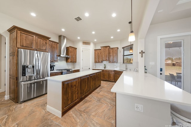 kitchen with tasteful backsplash, hanging light fixtures, appliances with stainless steel finishes, kitchen peninsula, and wall chimney range hood