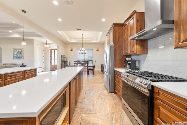 kitchen with a kitchen island, appliances with stainless steel finishes, hanging light fixtures, a tray ceiling, and wall chimney range hood