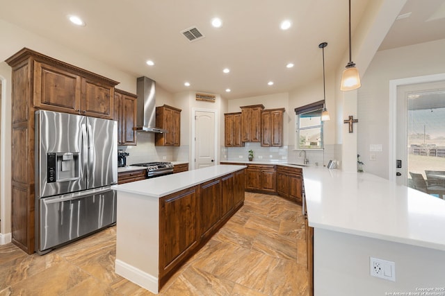 kitchen featuring appliances with stainless steel finishes, pendant lighting, sink, kitchen peninsula, and wall chimney range hood