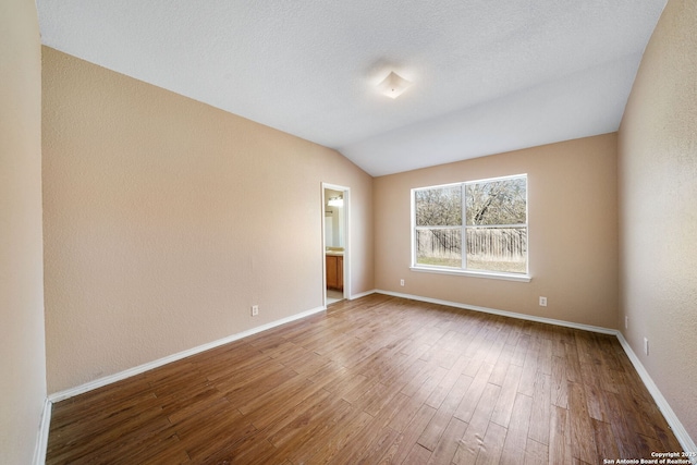 unfurnished room featuring wood-type flooring, lofted ceiling, and a textured ceiling