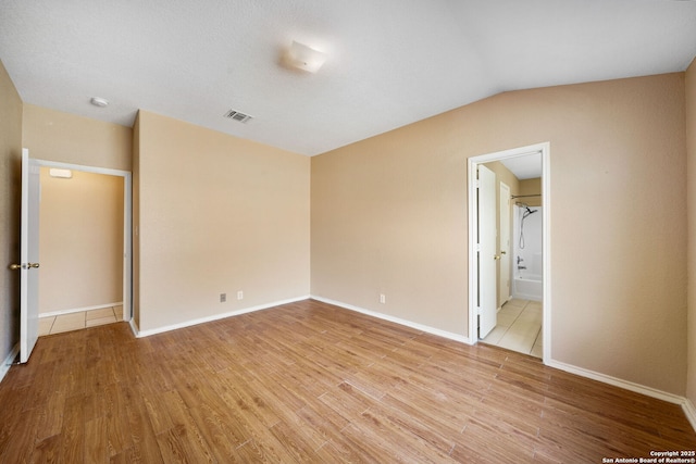 unfurnished bedroom featuring connected bathroom, vaulted ceiling, and light wood-type flooring