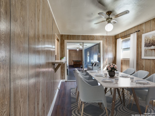 dining room featuring dark hardwood / wood-style floors, ceiling fan, and wood walls