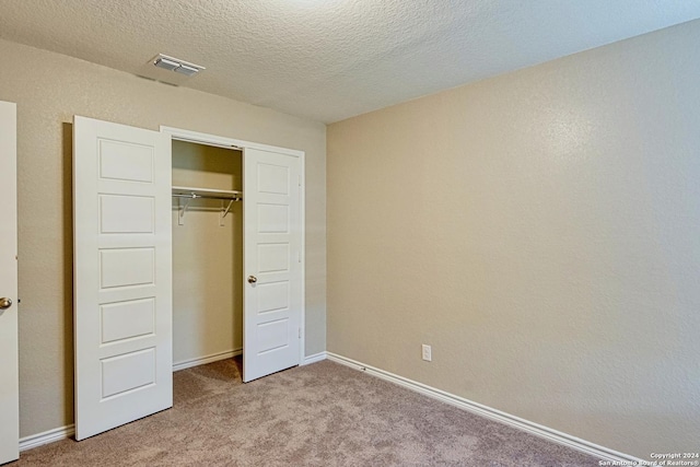 unfurnished bedroom featuring a closet, light carpet, and a textured ceiling