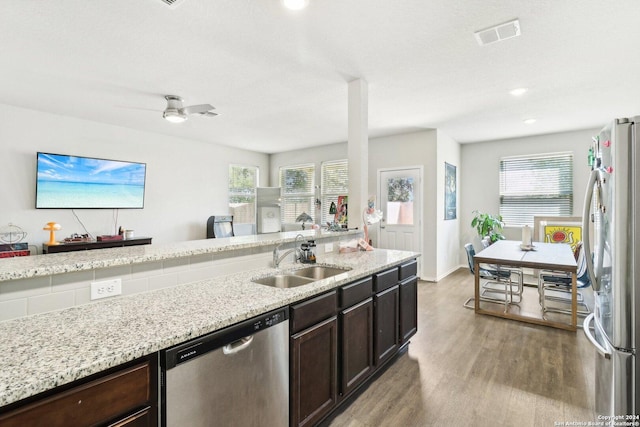 kitchen with sink, dark brown cabinets, stainless steel appliances, light hardwood / wood-style floors, and light stone countertops