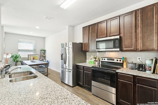 kitchen with sink, appliances with stainless steel finishes, dark brown cabinetry, tasteful backsplash, and light wood-type flooring