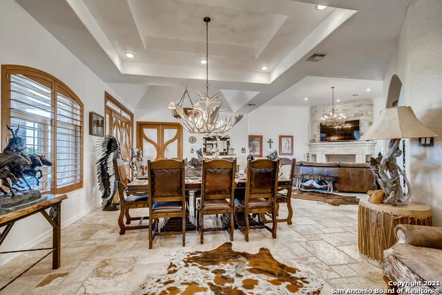 dining area featuring a raised ceiling, a large fireplace, and a chandelier