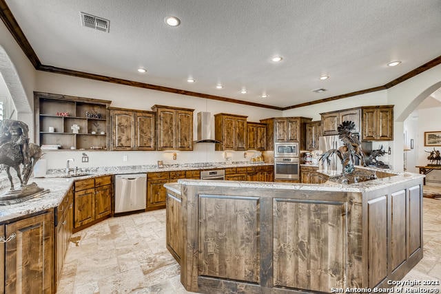 kitchen featuring a large island, sink, appliances with stainless steel finishes, a textured ceiling, and wall chimney exhaust hood