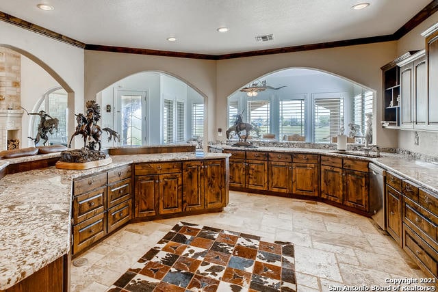 kitchen featuring light stone countertops, a wealth of natural light, stainless steel dishwasher, and sink