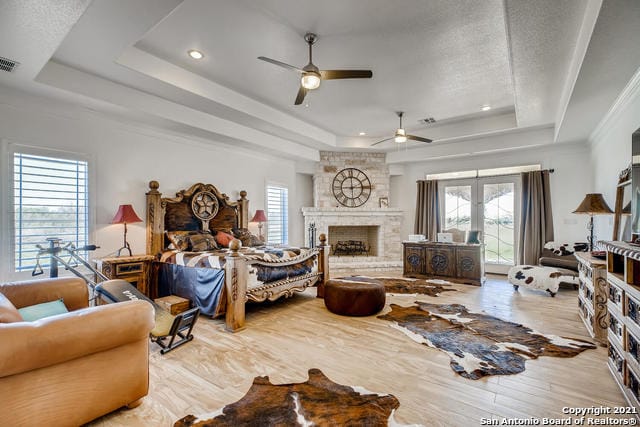 bedroom featuring a fireplace, a tray ceiling, and light hardwood / wood-style floors